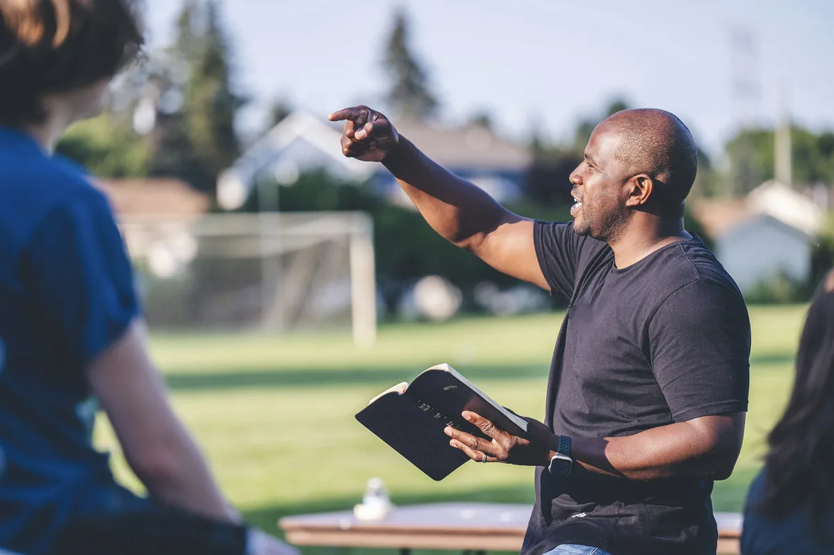 A church member with a Bible speaking outdoors at an outreach.